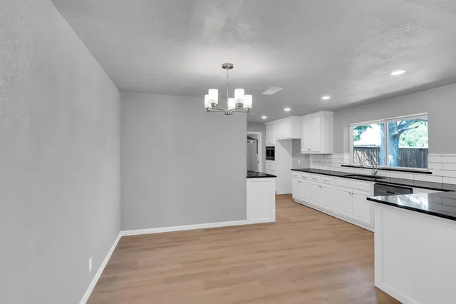 a large kitchen with granite countertop a stove a sink a refrigerator and white cabinets with wooden floor