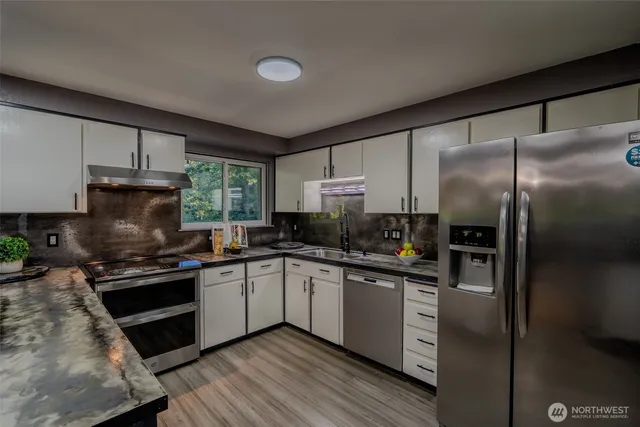 a kitchen with stainless steel appliances kitchen island granite countertop a refrigerator a sink dishwasher a stove and white cabinets with wooden floor