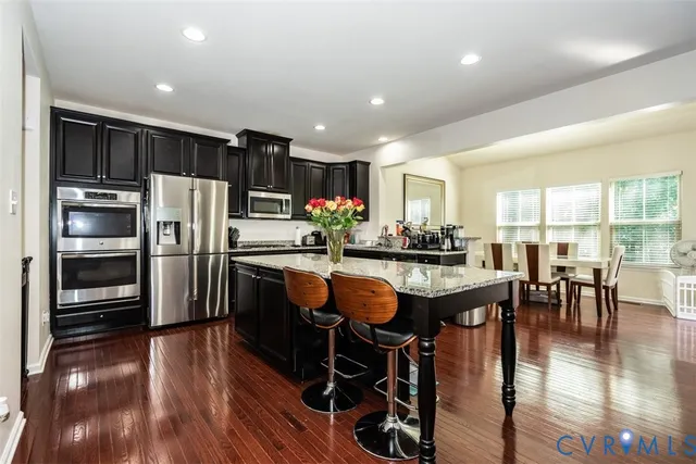 a kitchen with stainless steel appliances kitchen island granite countertop a refrigerator a stove a sink a dining table and chairs with wooden floor
