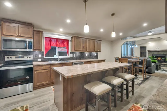 a kitchen with stainless steel appliances granite countertop a stove top oven a refrigerator a sink and chairs