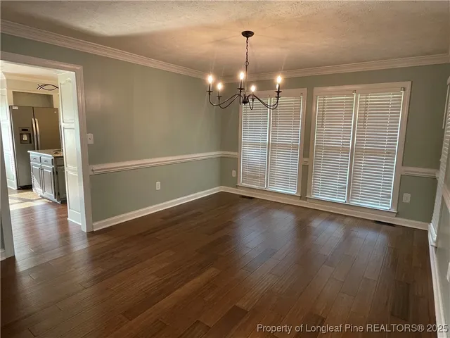 an empty room with wooden floor chandelier and windows
