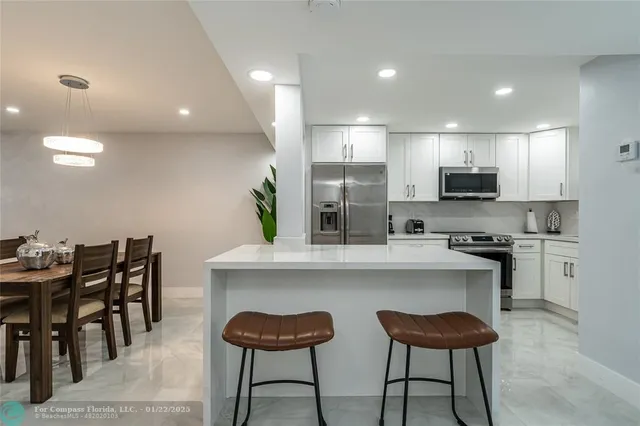 a kitchen with stainless steel appliances kitchen island granite countertop a dining table chairs and sink