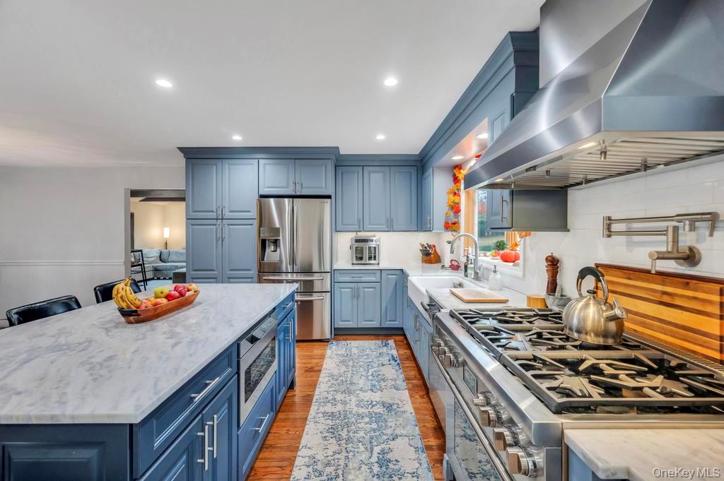 39 Bevin Road Northport, NY 11768 - Photo 13 of 44 Kitchen featuring wall chimney exhaust hood, dark wood-type flooring, blue cabinetry, appliances with stainless steel finishes, and light stone counters