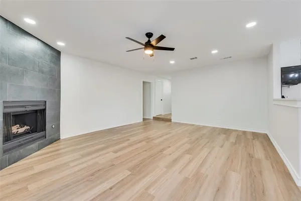 an empty room with wooden floor a ceiling fan a fireplace and windows