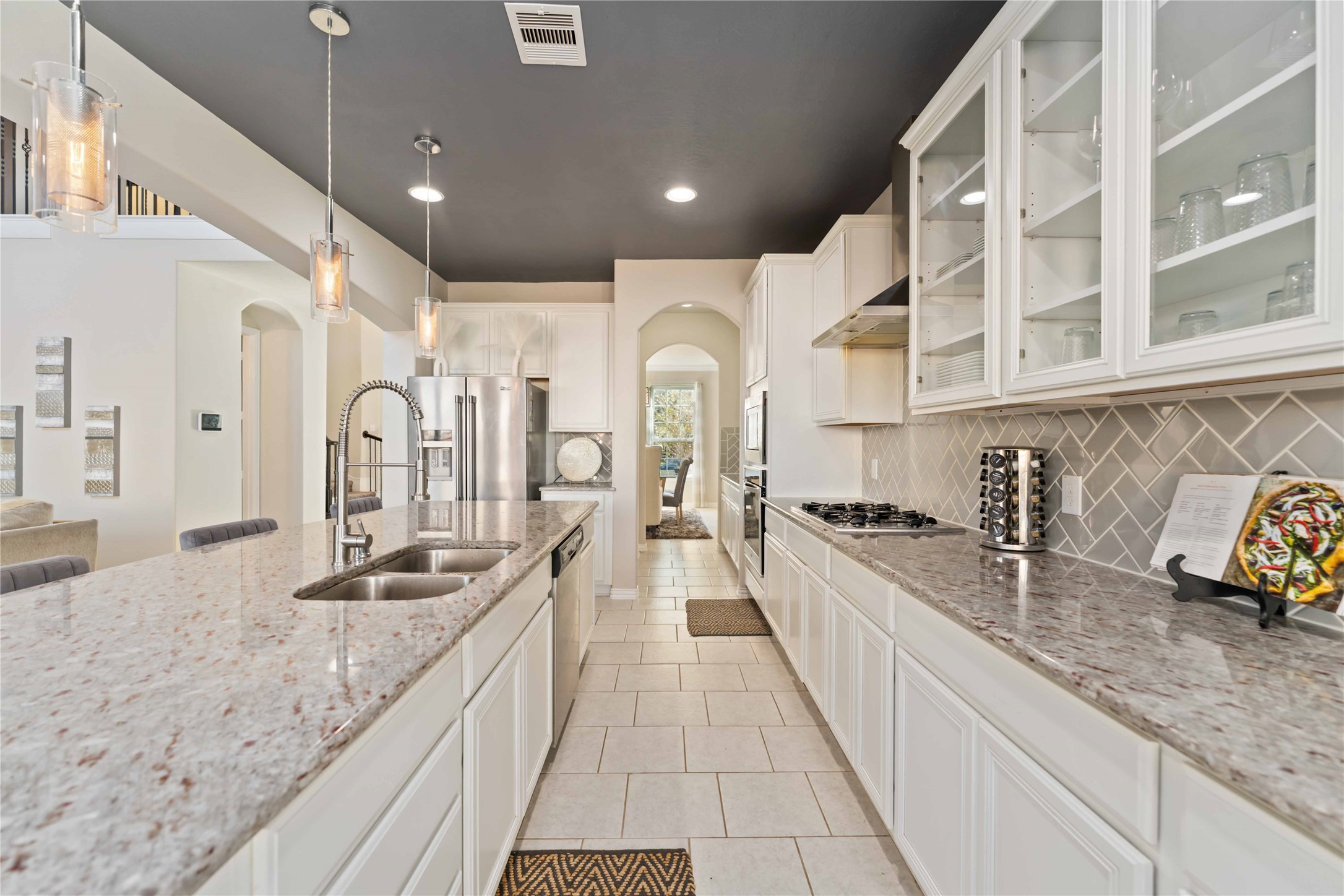 7403 Dry Stone Lane Rosenberg, TX 77469 - Photo 6 of 19 This gorgeous, light-filled kitchen is designed to be the heart of the home. With expansive countertops, a large center island, and abundant cabinetry, it offers the perfect balance of style and function—whether you’re cooking for family, hosting friends, or enjoying a quiet morning at home. Pendant lighting, glass front cabinetry, and open sightlines keep the space feeling bright, connected, and effortlessly inviting.