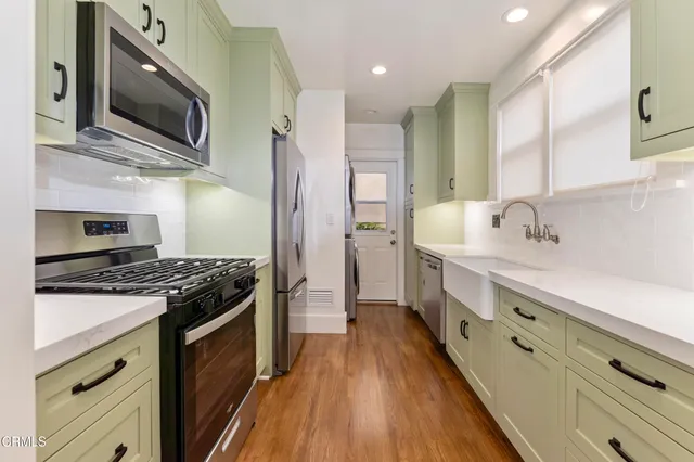 a kitchen with stainless steel appliances a sink dishwasher a stove top oven a refrigerator with wooden floor and cabinets