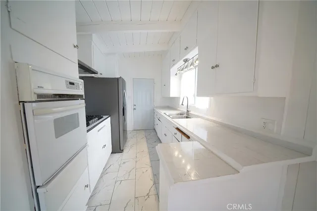 a kitchen with granite countertop a refrigerator a sink a stove and white cabinets