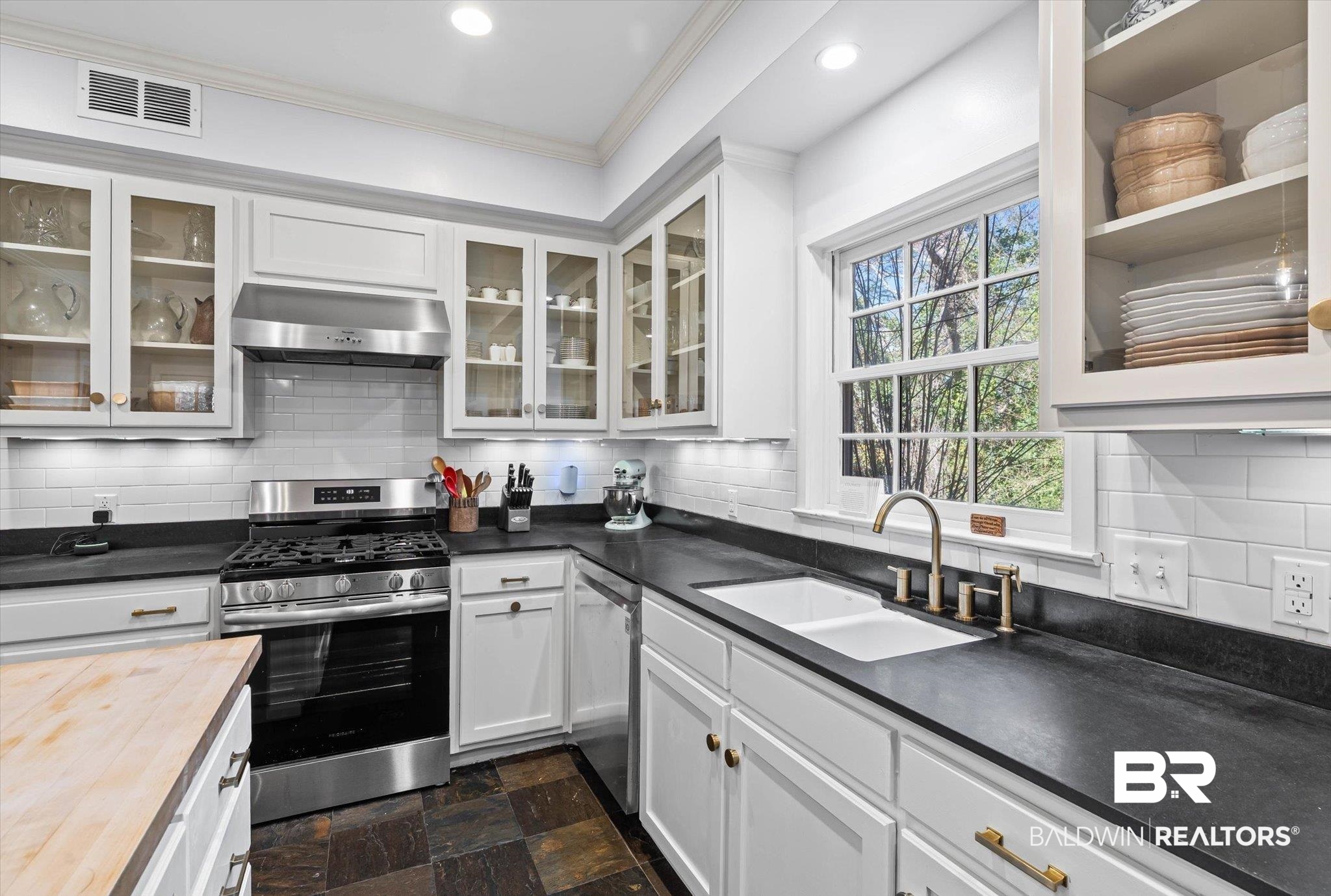 4776 Falls Church Road Mobile, AL 36608 - Photo 9 of 45 Kitchen featuring white cabinetry, dark countertops, a stainless steel range with matching vent hood, an undermount sink with a brass-finish faucet, and a subway tile backsplash