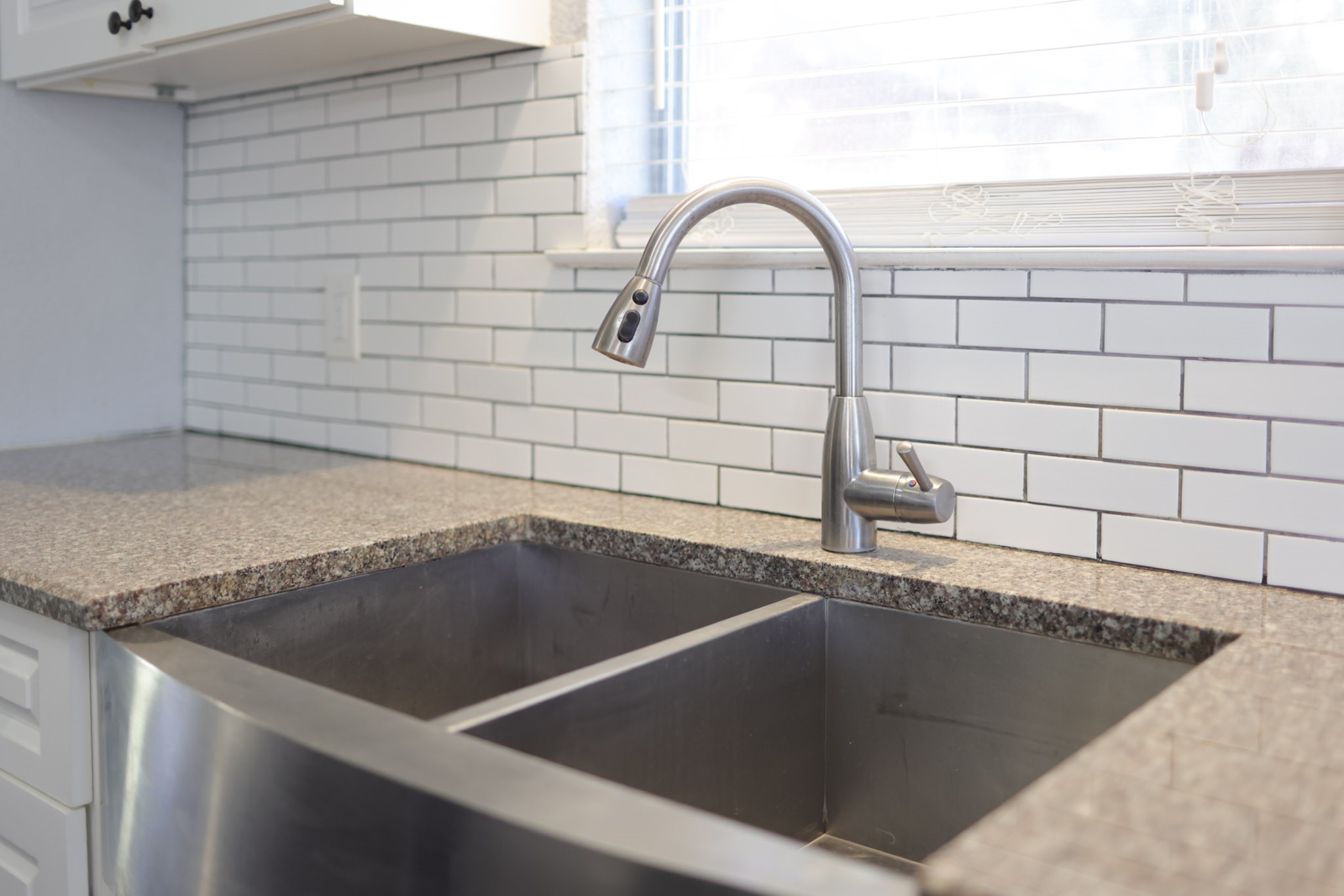 407 Tamarind Street Lake Jackson, TX 77566 - Photo 13 of 36 This kitchen features a modern stainless steel double sink with a sleek faucet, set against a stylish white subway tile backsplash and granite countertop, offering a clean and contemporary look.