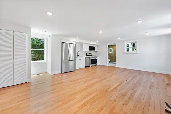 a view of empty room with wooden floor and kitchen