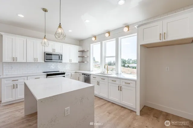 a kitchen with kitchen island granite countertop a stove a sink a center island a refrigerator and white cabinets with wooden floor