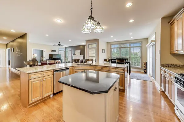 a kitchen with stainless steel appliances granite countertop a stove a refrigerator a kitchen island a dining table and chairs with wooden floor