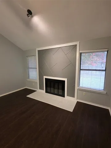 an empty room with wooden floor a ceiling fan a fireplace and windows