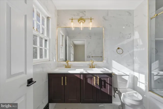 a bathroom with a granite countertop sink a toilet a mirror and shower