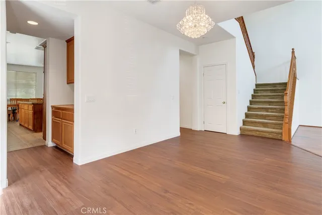 a view of an empty room with wooden floor and a kitchen