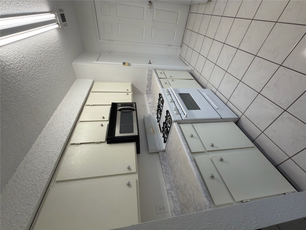 Kitchen with white gas range, light countertops, white cabinetry, a textured ceiling, and stainless steel microwave