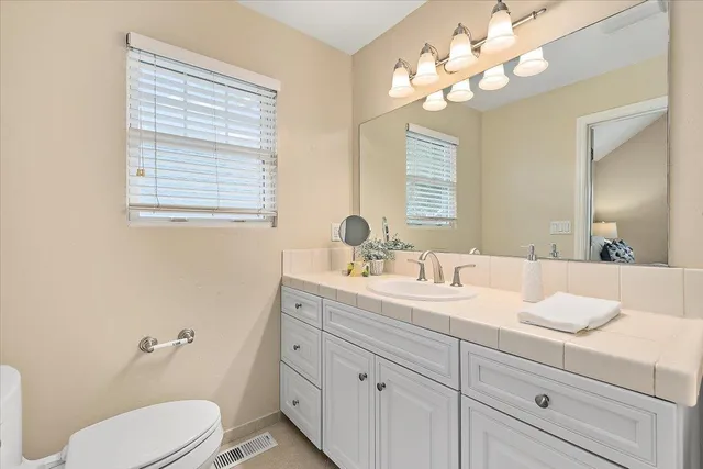 a bathroom with a toilet a sink a mirror a window and vanity