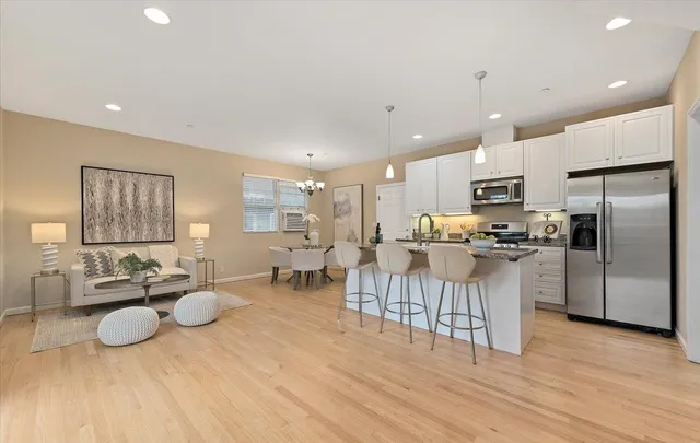 a kitchen with stainless steel appliances kitchen island granite countertop a refrigerator a stove a sink a dining table and chairs with wooden floor