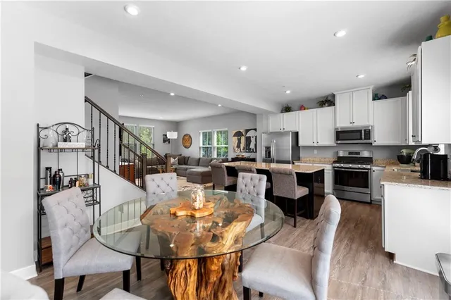 a kitchen with stainless steel appliances kitchen island granite countertop a stove a sink a dining table and chairs with wooden floor