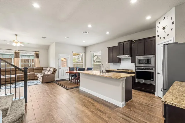 a kitchen with stainless steel appliances a stove top oven a refrigerator a dining table and chairs