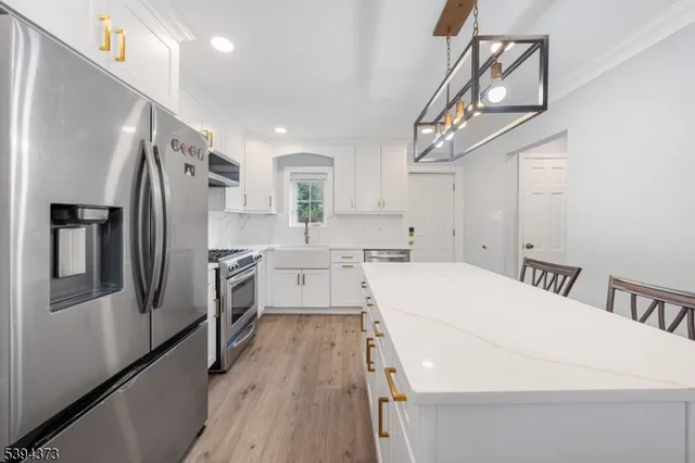 a kitchen with stainless steel appliances a refrigerator a sink dishwasher a stove and white cabinets with wooden floor