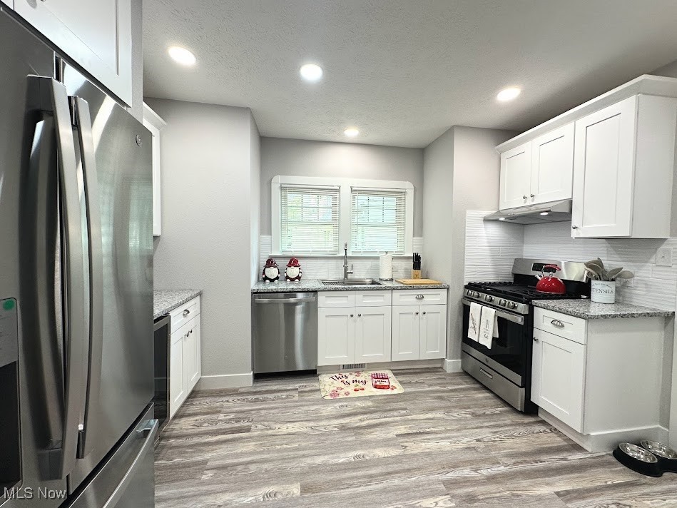 3190 Warrington Road Cleveland, OH 44120 - Photo 9 of 21 Kitchen featuring stainless steel appliances, a textured ceiling, white cabinets, light wood-style flooring, and tasteful backsplash