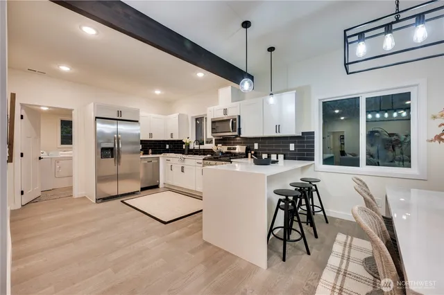 a kitchen with stainless steel appliances kitchen island granite countertop a refrigerator a stove a sink dishwasher and white cabinets with wooden floor