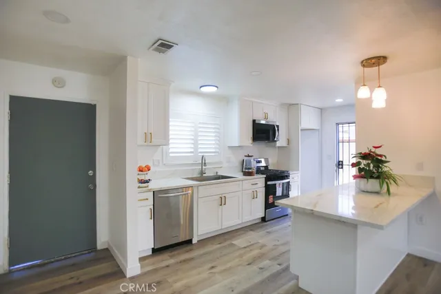 a kitchen with stainless steel appliances a sink a stove a refrigerator cabinets and wooden floor