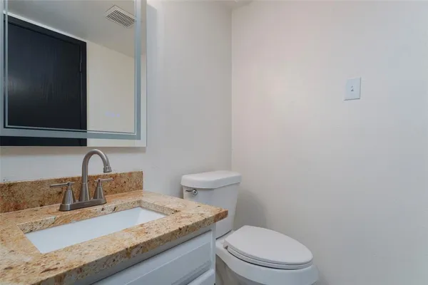 a bathroom with a granite countertop toilet sink and mirror