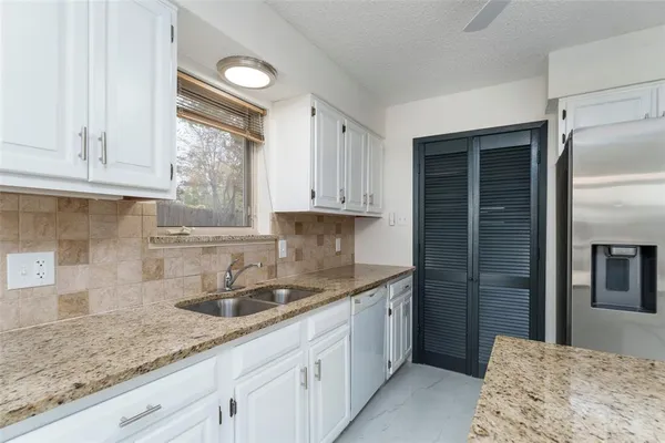 a kitchen with granite countertop a sink stainless steel appliances white cabinets and a window