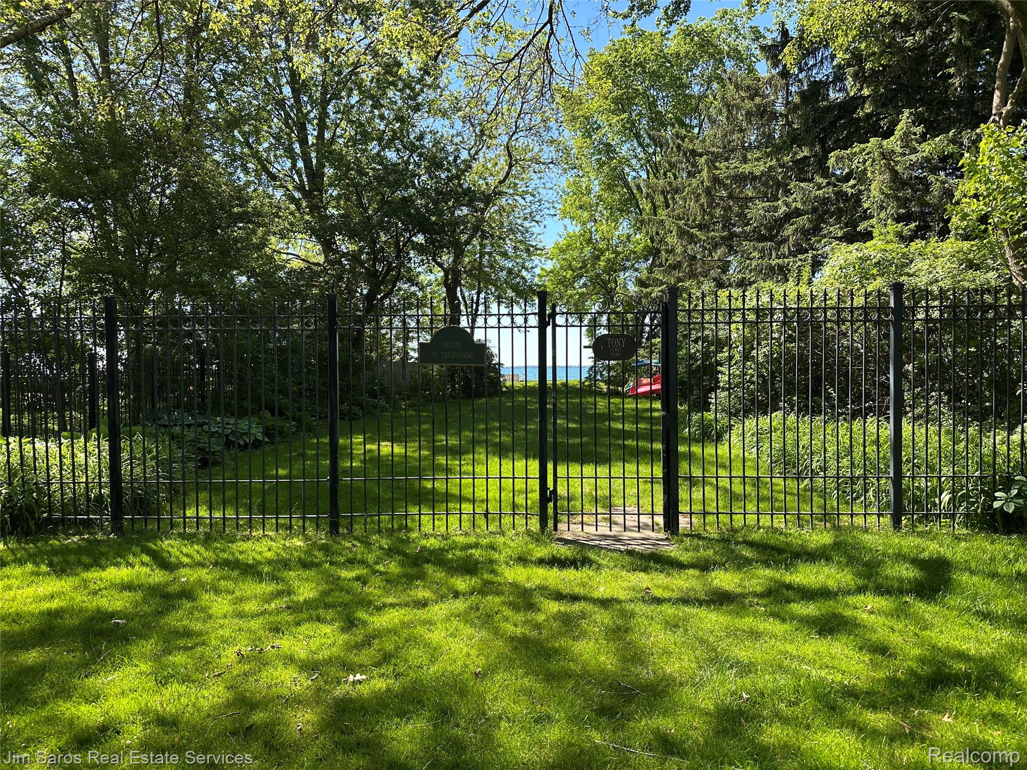 910 Edgemont Park Grosse Pointe, MI 48230 - Photo 51 of 56 Manicured lawn area featuring a wrought iron fence and gate, mature trees, and visible waterbody beyond