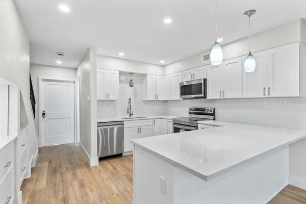 a view of an empty room with wooden floor and a kitchen