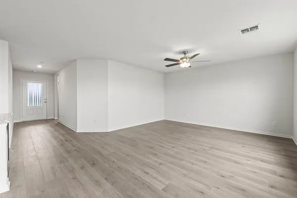 a view of an empty room with wooden floor and a ceiling fan