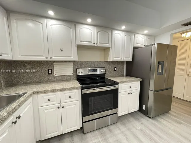 a kitchen with stainless steel appliances granite countertop a refrigerator a stove a sink and white cabinets