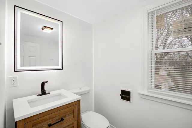 a bathroom with a toilet a sink a mirror and a window