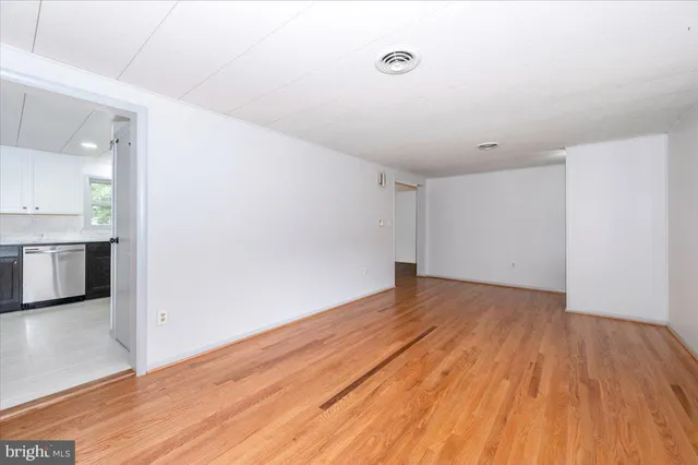 a view of empty room with wooden floor and kitchen
