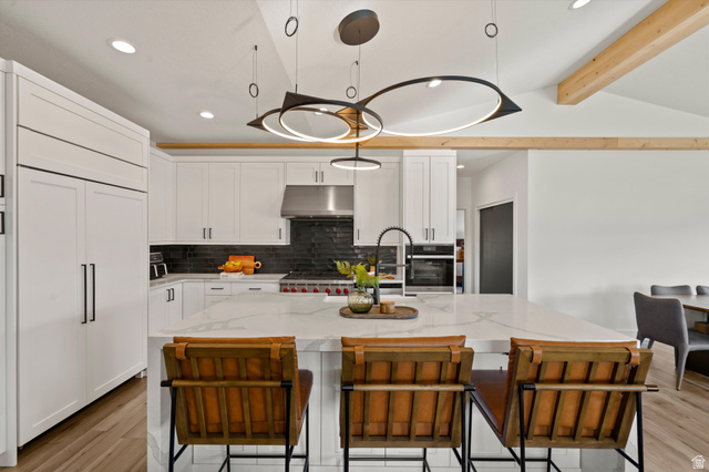4499 North Seven Bridges Road, Unit 9 Eden, UT 84310 - Photo 9 of 65 White cabinetry, stainless steel appliances, dark tile backsplash, a center island with countertop seating, and exposed wood ceiling beams
