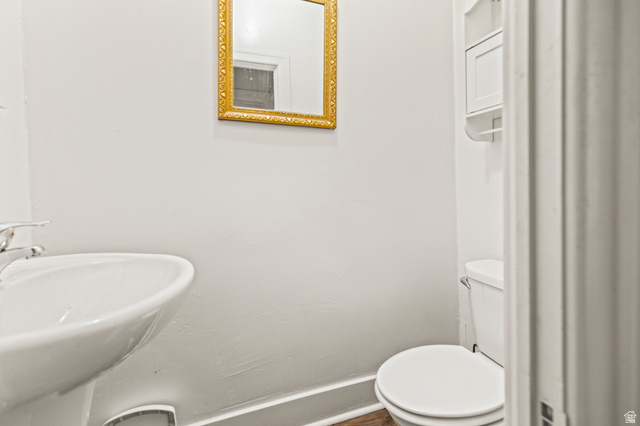 69 South Main Street Manti, UT 84642 - Photo 19 of 44 Pedestal sink with chrome faucet, gold-framed mirror, white wall-mounted storage, toilet, and wood-finish flooring