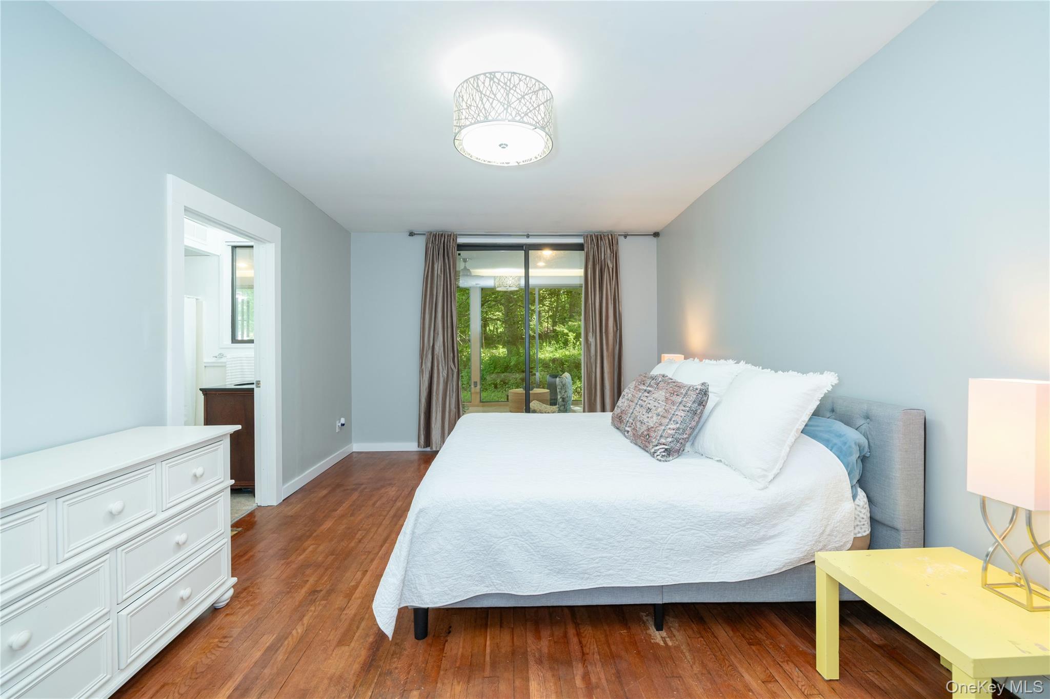 4 Half Mile Road Armonk, NY 10504 - Photo 12 of 28 Spacious primary bedroom with warm hardwood floors, high ceilings, serene natural light, and sliding glass doors leading directly to a screened porch overlooking the peaceful wooded property.