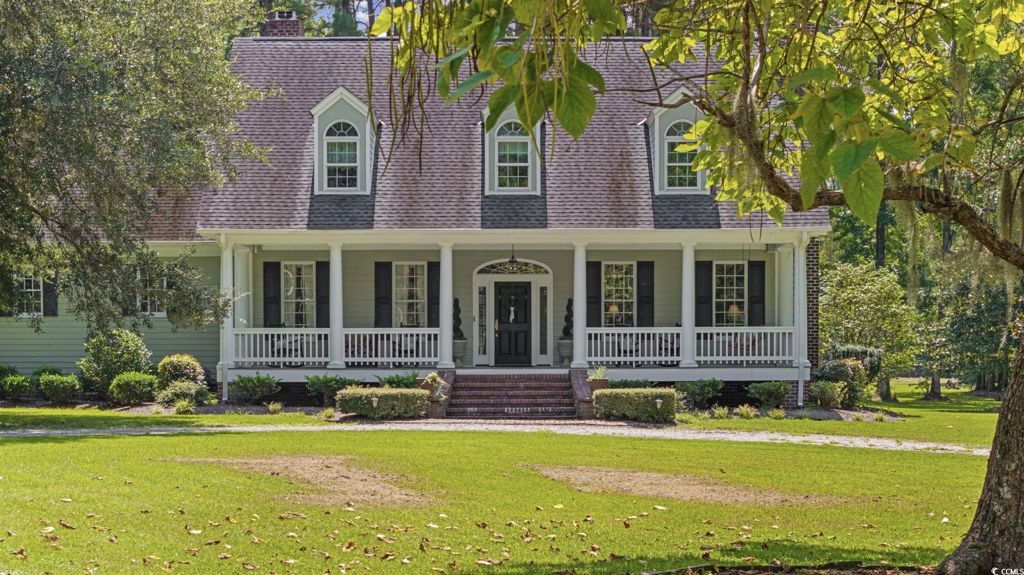 Cape cod home featuring roof with shingles, a porch, a front yard, and a chimney