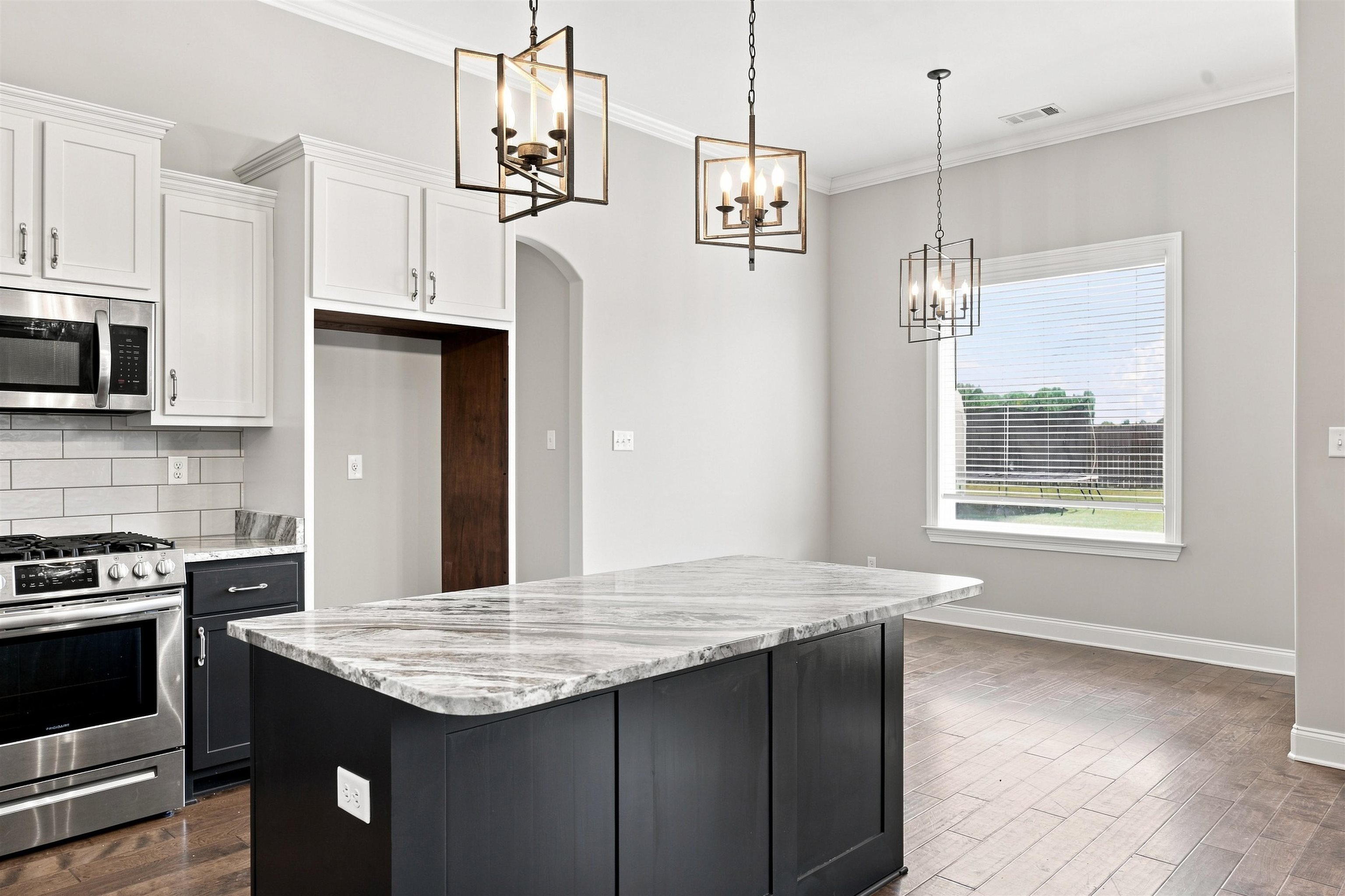 70 Trinity Cove Atoka, TN 38004 - Photo 5 of 19 Kitchen featuring a large island with a substantial countertop, white cabinetry, subway tile backsplash, stainless steel appliances, and wood-finish flooring