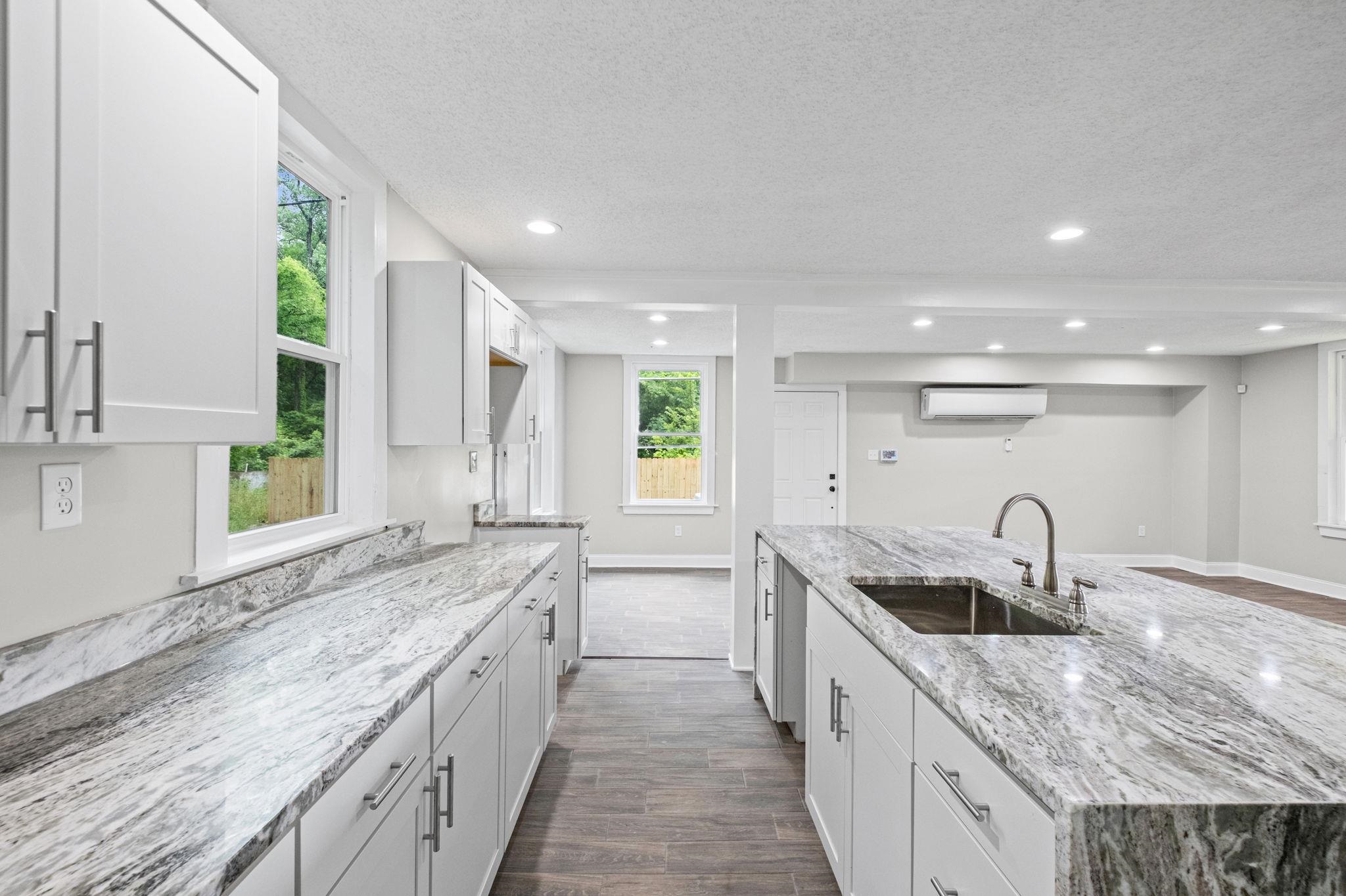 5843 Stewart Road Lakeland, TN 38002 - Photo 14 of 26 Kitchen featuring a large island with an undermount sink and gooseneck faucet, white shaker cabinetry, patterned stone countertops, and wood-finish flooring