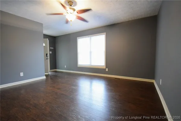 an empty room with wooden floor chandelier fan and windows