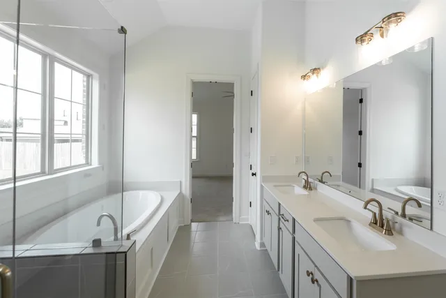 a bathroom with a tub sink double vanity granite tub shower and mirror
