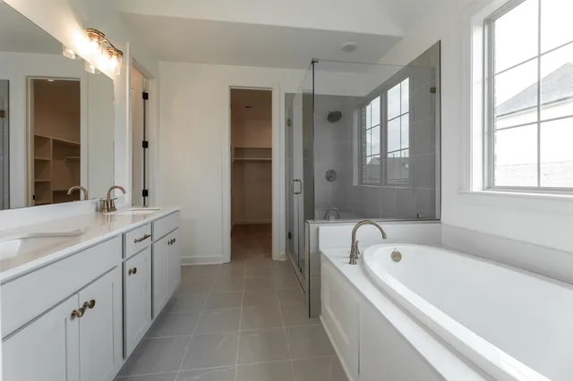 a bathroom with a bathtub a double vanity sink a vanity a window and a mirror