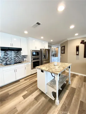 a large kitchen with stainless steel appliances a stove a sink dishwasher and a refrigerator with wooden floor