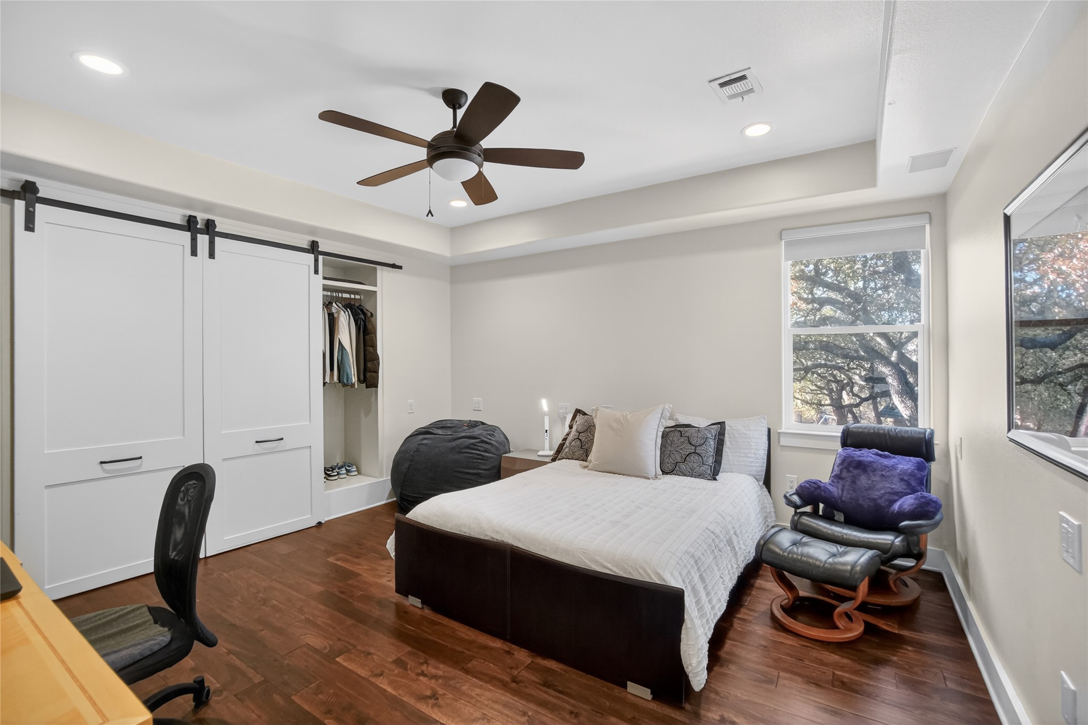 3627 Stoneridge Road Austin, TX 78746 - Photo 18 of 40 Bedroom with a barn door, dark wood finished floors, recessed lighting, ceiling fan, and a tray ceiling