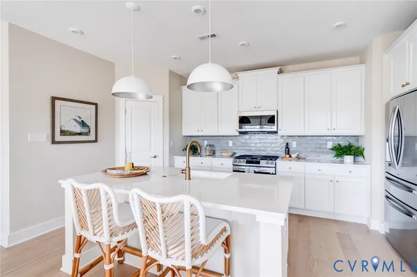 a kitchen with stainless steel appliances kitchen island granite countertop a refrigerator a stove a sink a dining table and chairs with wooden floor