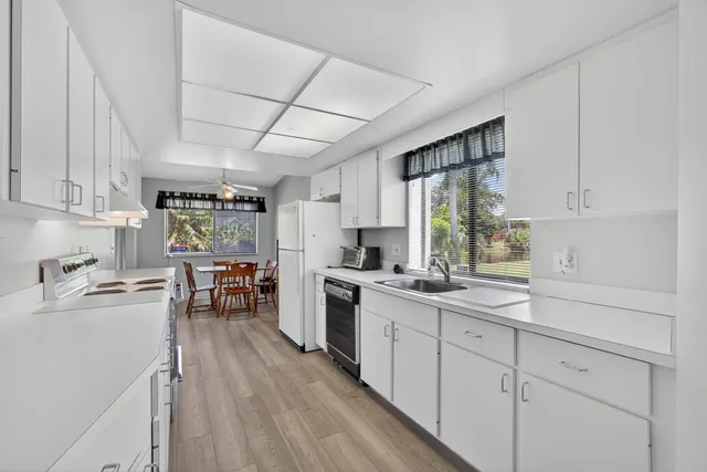 a kitchen with granite countertop a sink dishwasher stove and white cabinets with wooden floor