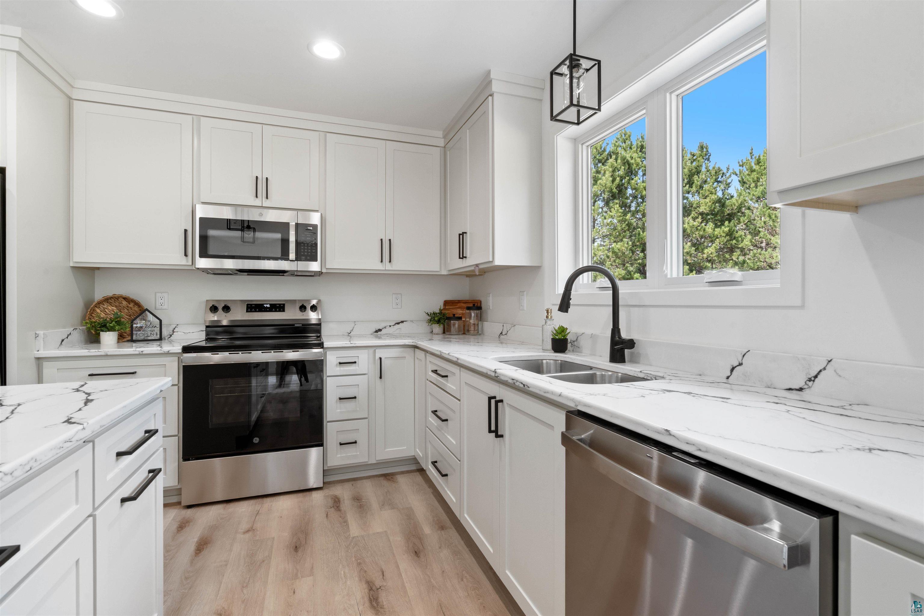 1386 Stephen Road Cloquet, MN 55720 - Photo 6 of 25 Kitchen featuring white cabinetry, wood-finish flooring, stainless steel appliances, a double basin sink with a black faucet, and white countertops with black veining